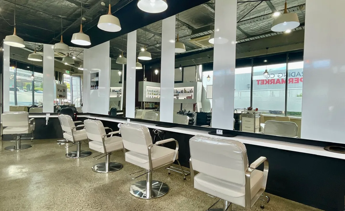 A row of white styling chairs facing mirrors under pendant lights inside Groove Hair