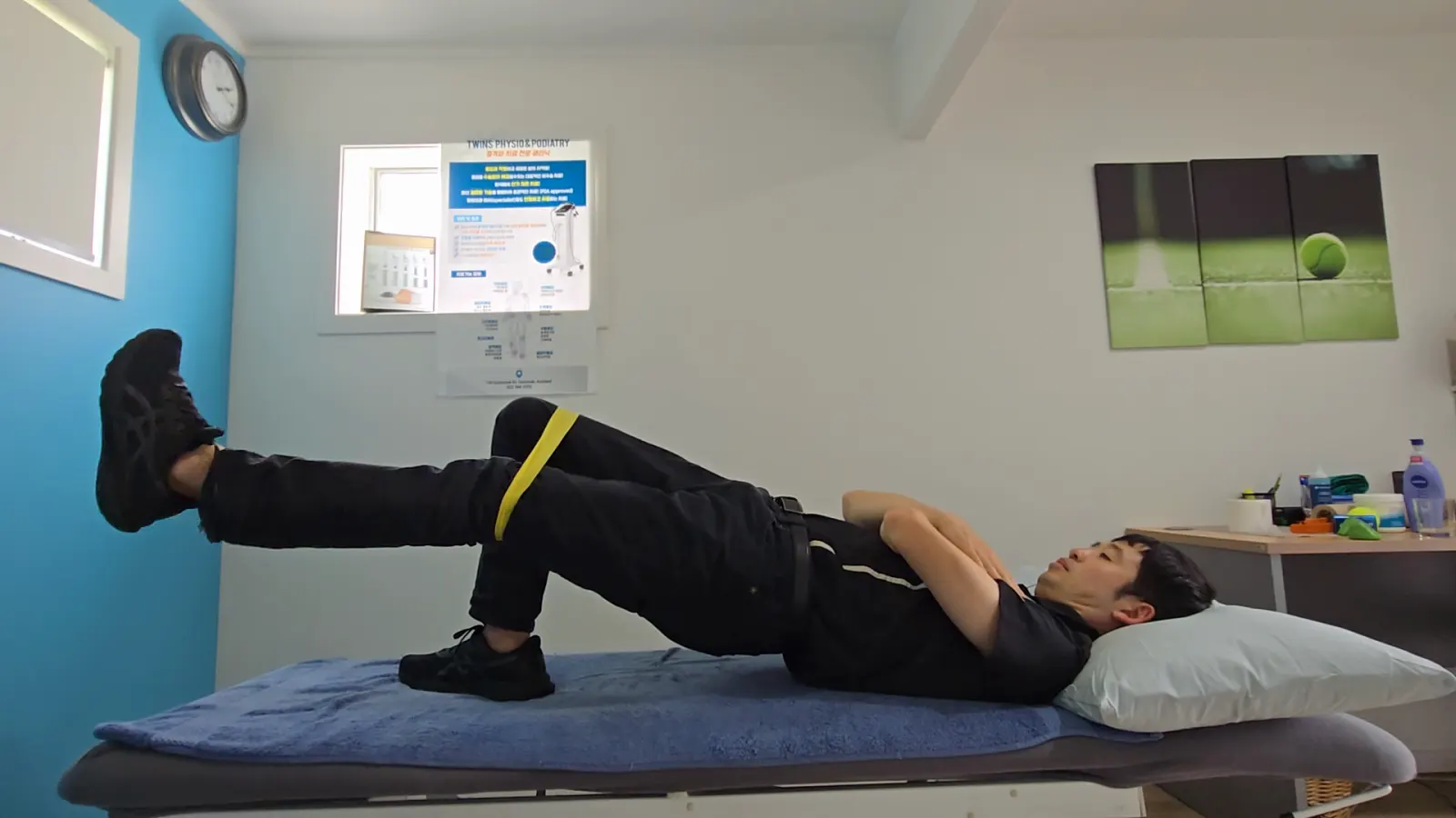 A Twins Physio & Podiatry clinician demonstrating a single-leg bridge with a resistance band, from the clinic's own exercise video